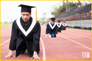 Four young men are kneeled down on the a track and field while dressed in graduation robes. 