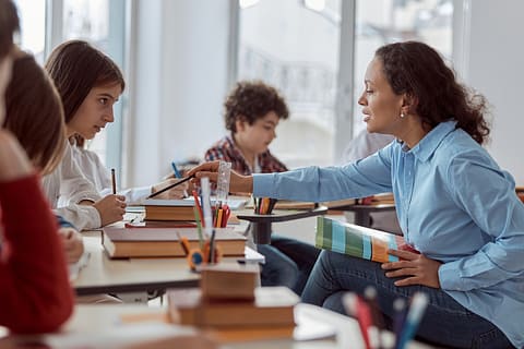 A teacher explaining a topic to her student, emphasizing the importance of teacher pay.
