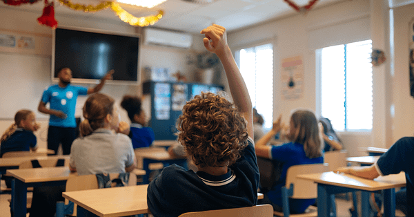 Young boy raises his hand in a classroom.
