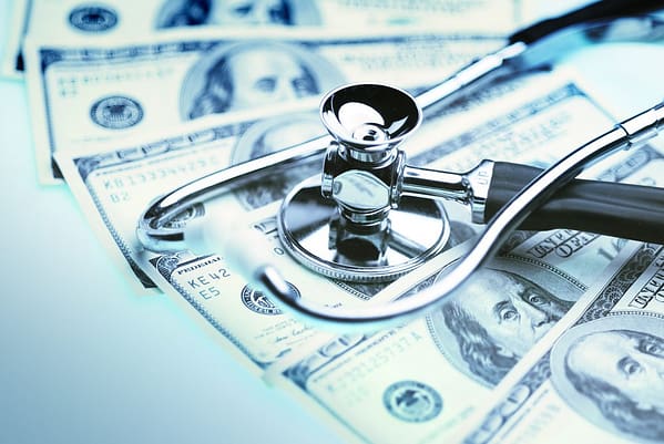 A doctor's stethoscope is laid on top of hundred dollar bills. It figuratively represents healthy and unhealthy markets.